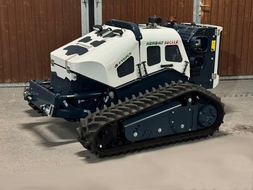 Ein weiß-schwarzer Traktor mit schwarzen Ketten steht vor einem Holzgebäude.