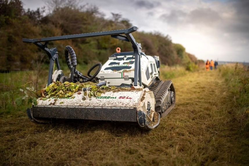 Ein weiß-schwarzer Traktor schneidet Gras auf einem Feld.