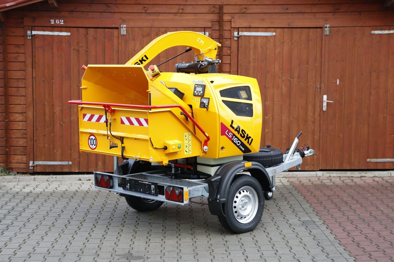 Vor einer Holzgarage steht eine gelbe Maschine.