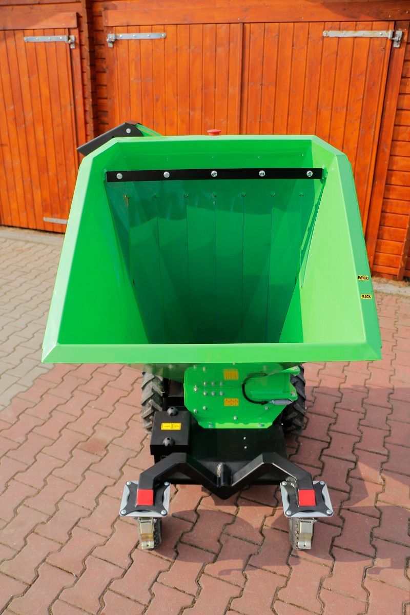 Ein grüner Muldenkipper parkt auf einem gepflasterten Gehweg vor einer Holzgarage.