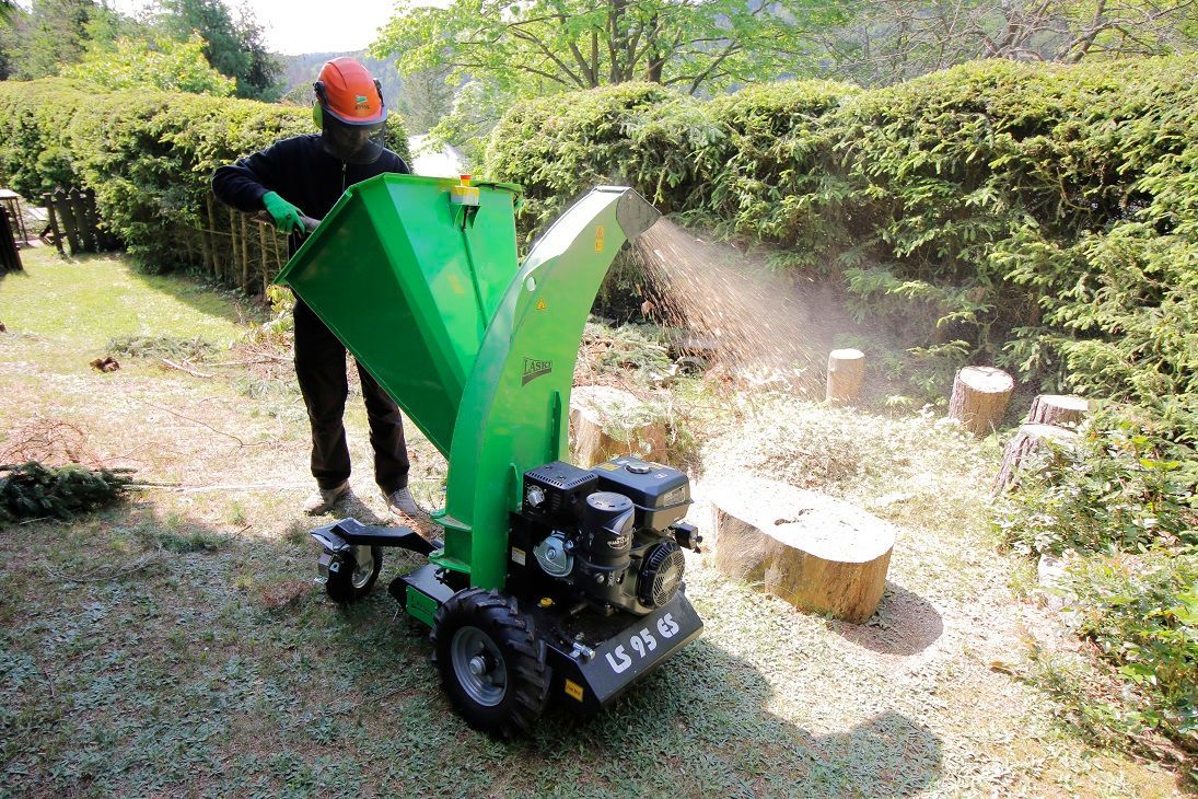 Ein Mann benutzt eine grüne Maschine zum Zerkleinern von Bäumen.