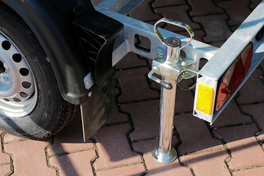 Ein Anhänger ist auf einem gepflasterten Gehweg neben einem Reifen geparkt.