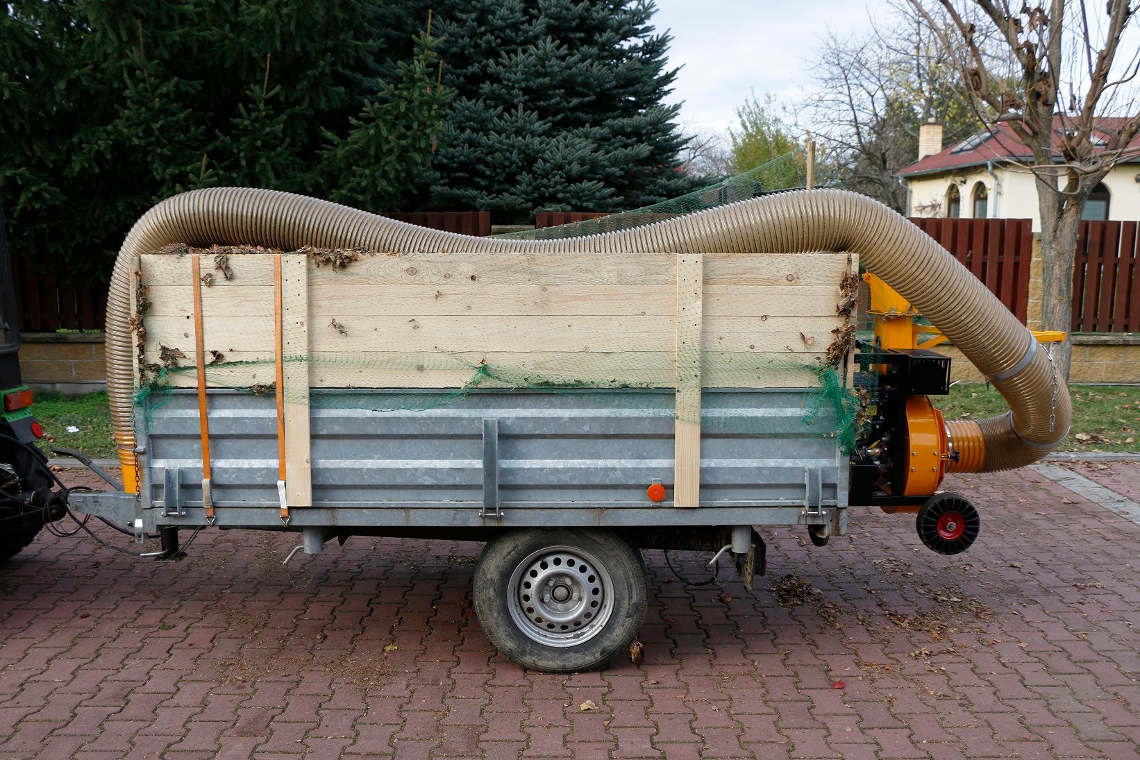 Auf einem gepflasterten Gehweg ist ein Anhänger mit einem daran befestigten Schlauch geparkt.