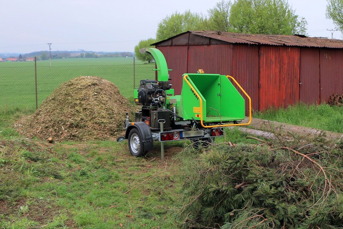 Ein grüner Baumhäcksler steht auf einem Feld neben einem Haufen Holzspäne.