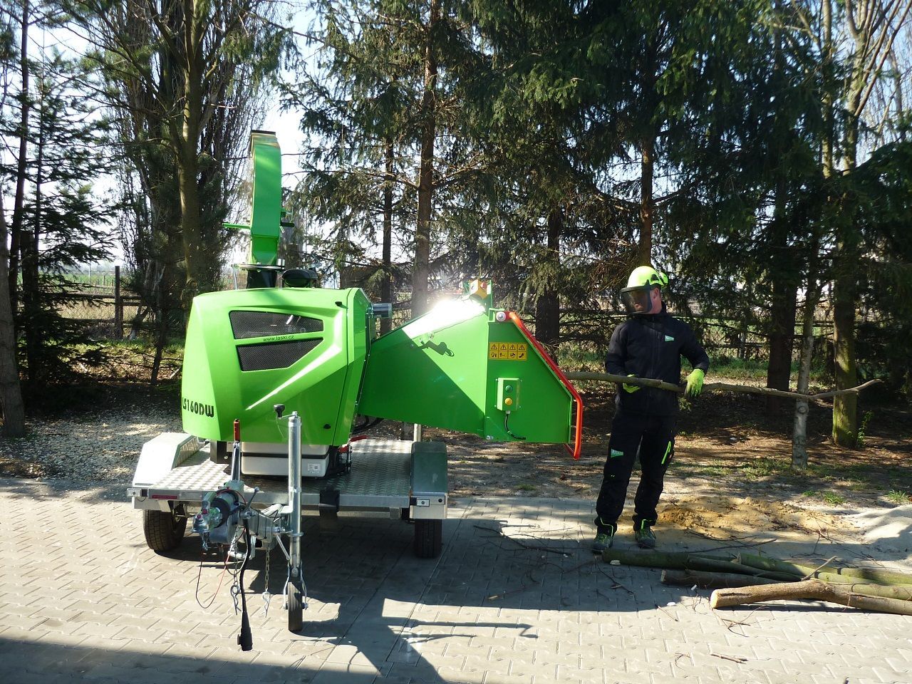 Ein Mann steht neben einer grünen Maschine, die auf einem Anhänger steht.