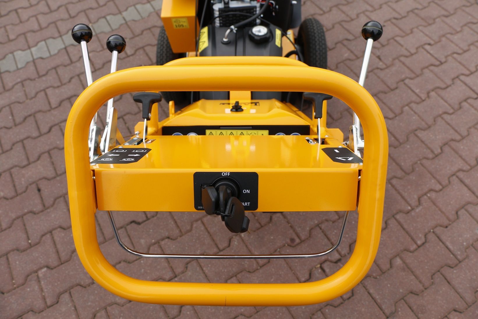 Ein gelber Rasenmäher steht auf einem gepflasterten Gehweg