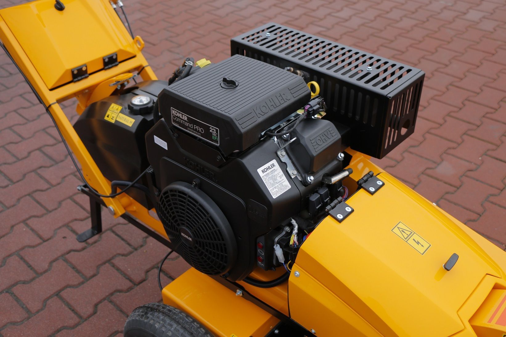 Ein gelber Rasenmäher mit schwarzem Motor steht auf einem gepflasterten Gehweg.