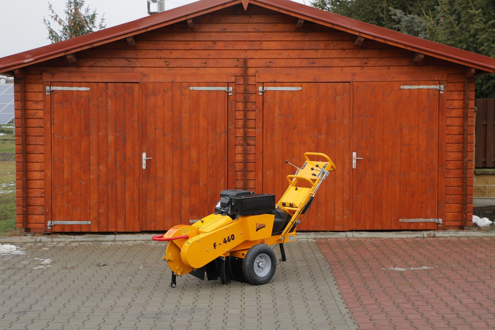 Vor einer Holzgarage steht eine gelbe Maschine.