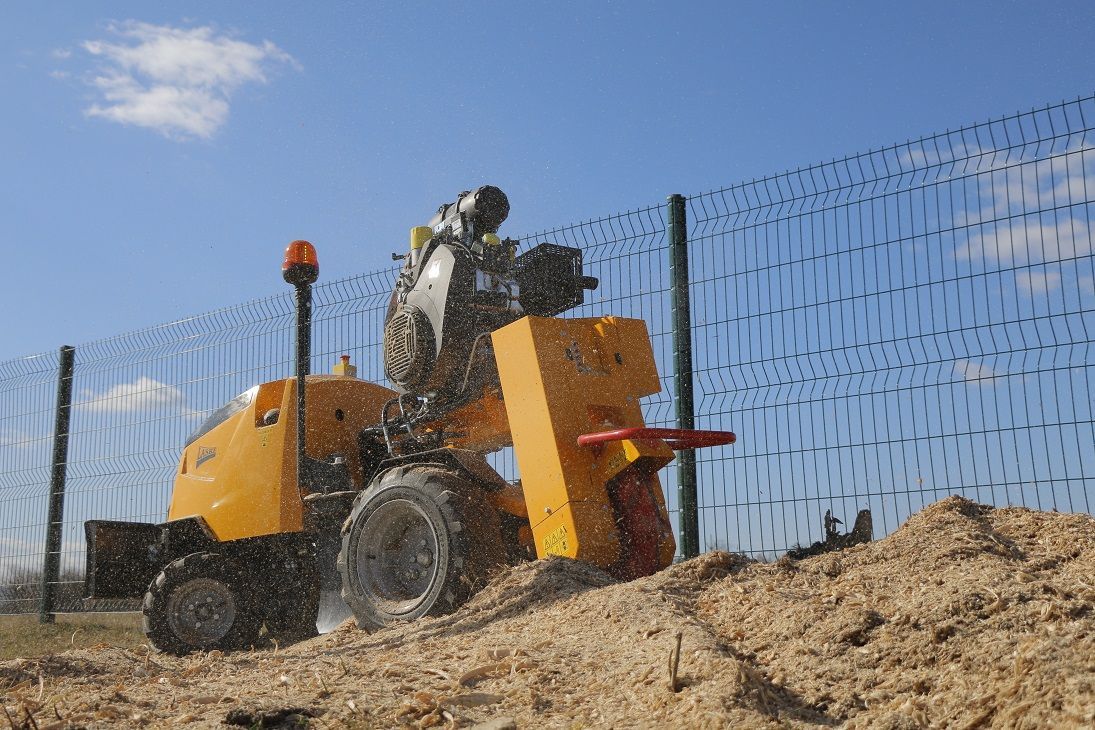 Ein Mann fährt mit einem gelben Traktor durch den Dreck in der Nähe eines Zauns.