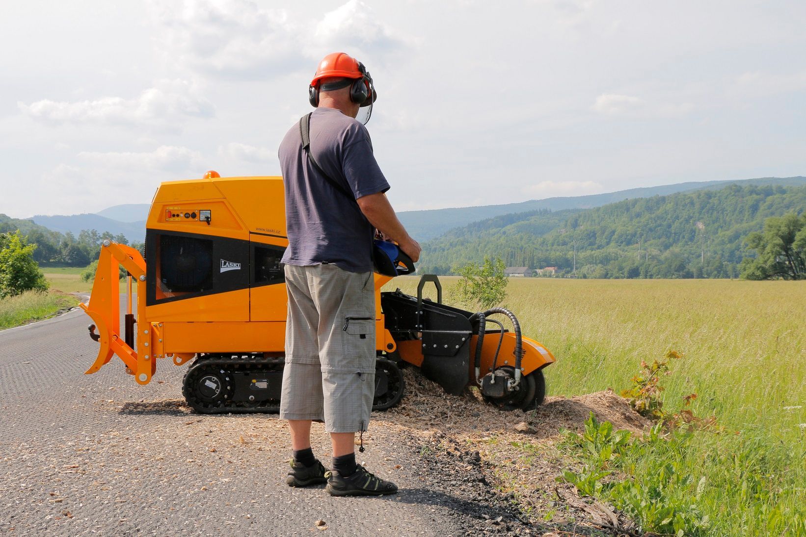 Ein Mann steht neben einer gelben Maschine am Straßenrand.
