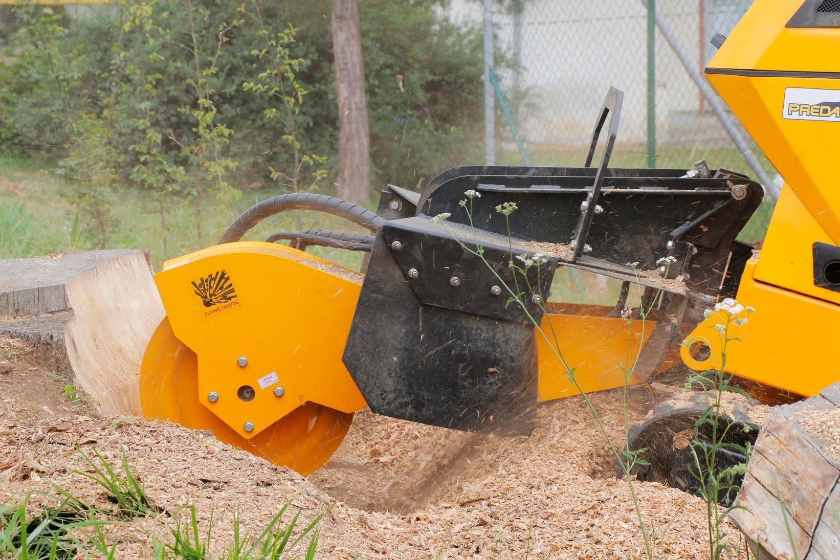 Ein gelber Traktor fräst einen Baumstumpf.