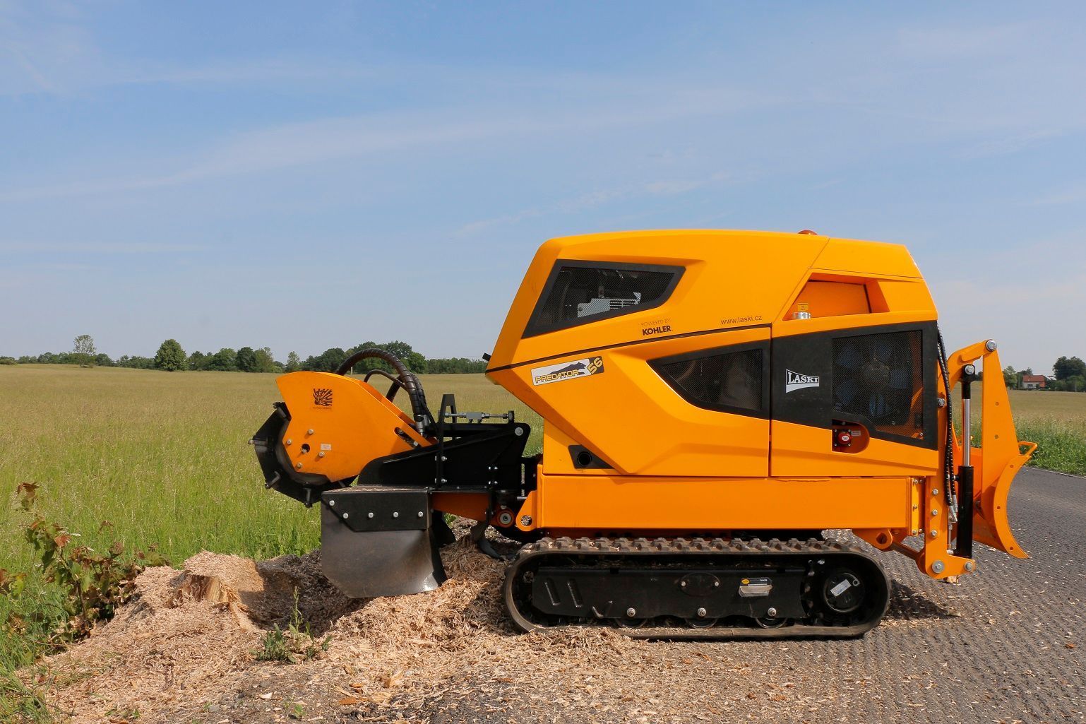 Ein gelber Traktor schneidet auf einem Feld einen Baumstumpf ab.