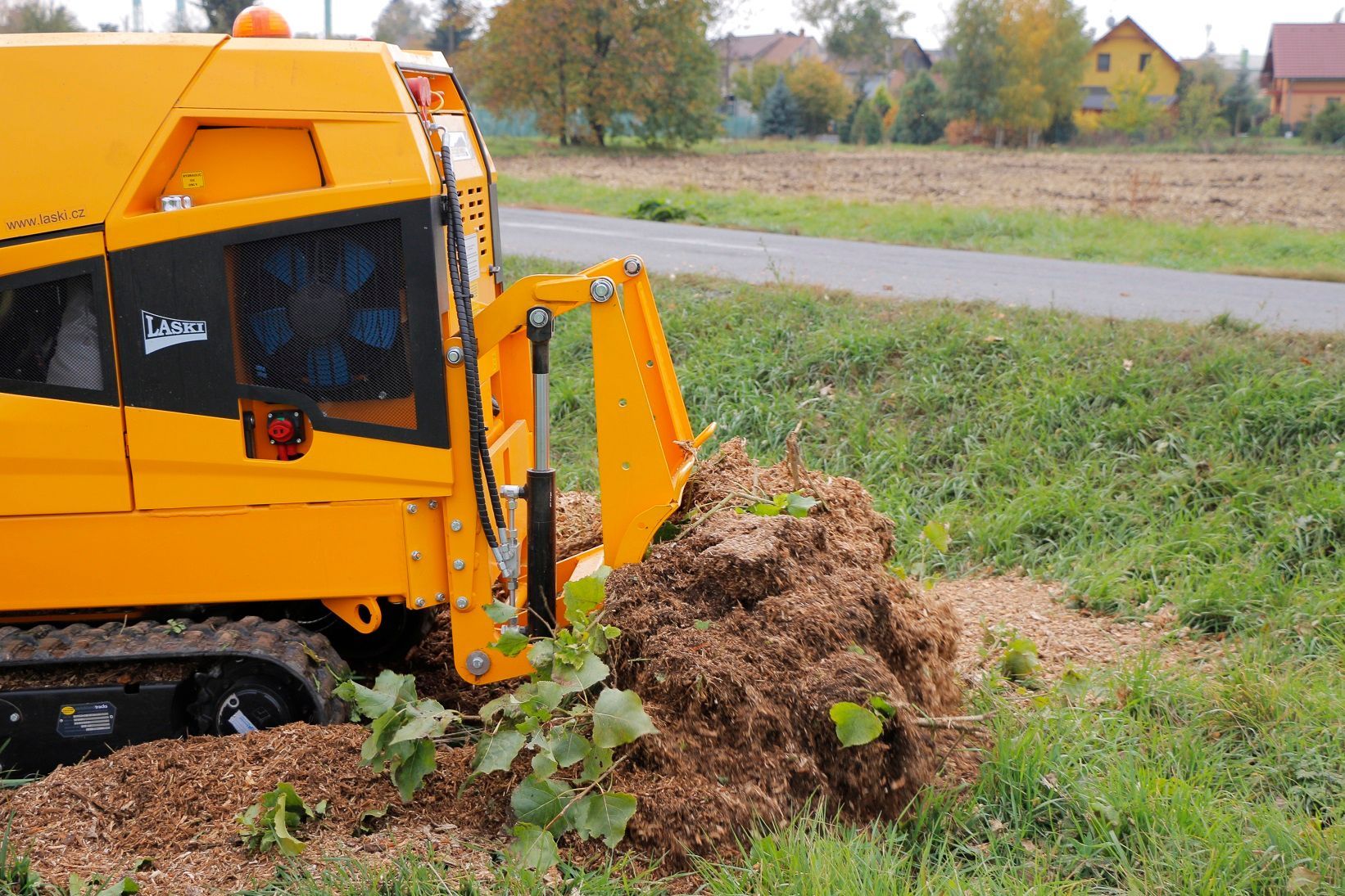 Ein gelber Traktor schneidet auf einem Feld einen Baumstumpf ab.