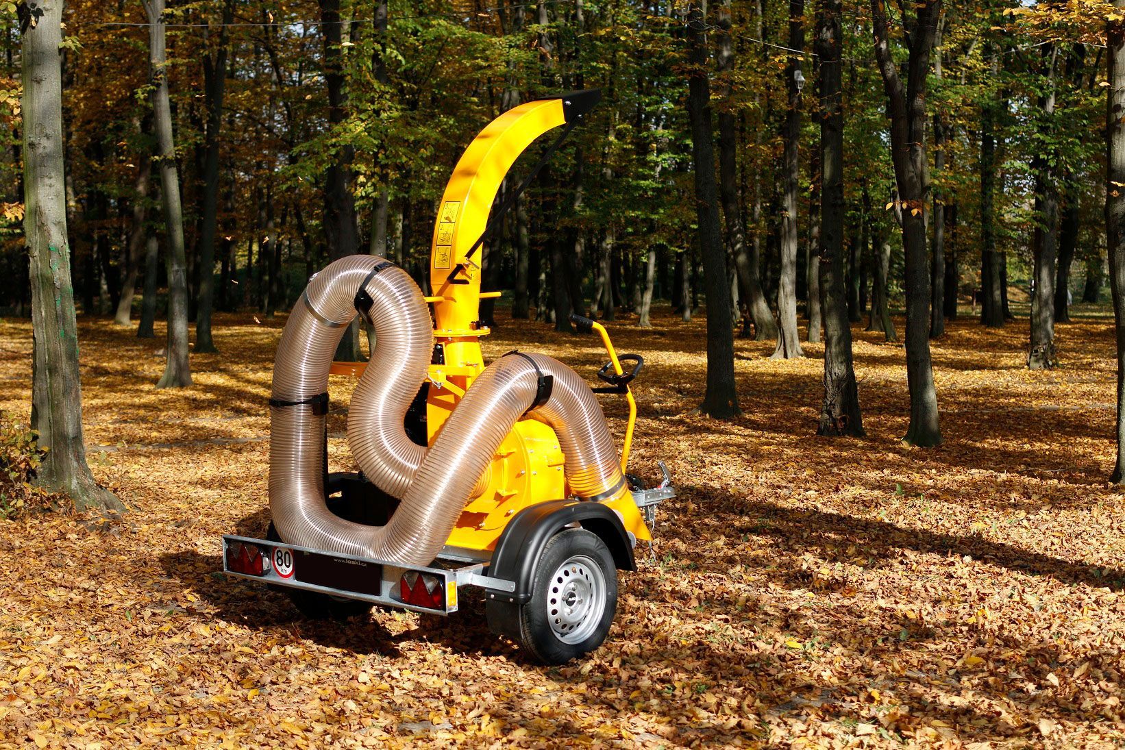 Ein gelber Laubsauger steht auf einem Anhänger mitten in einem Wald.