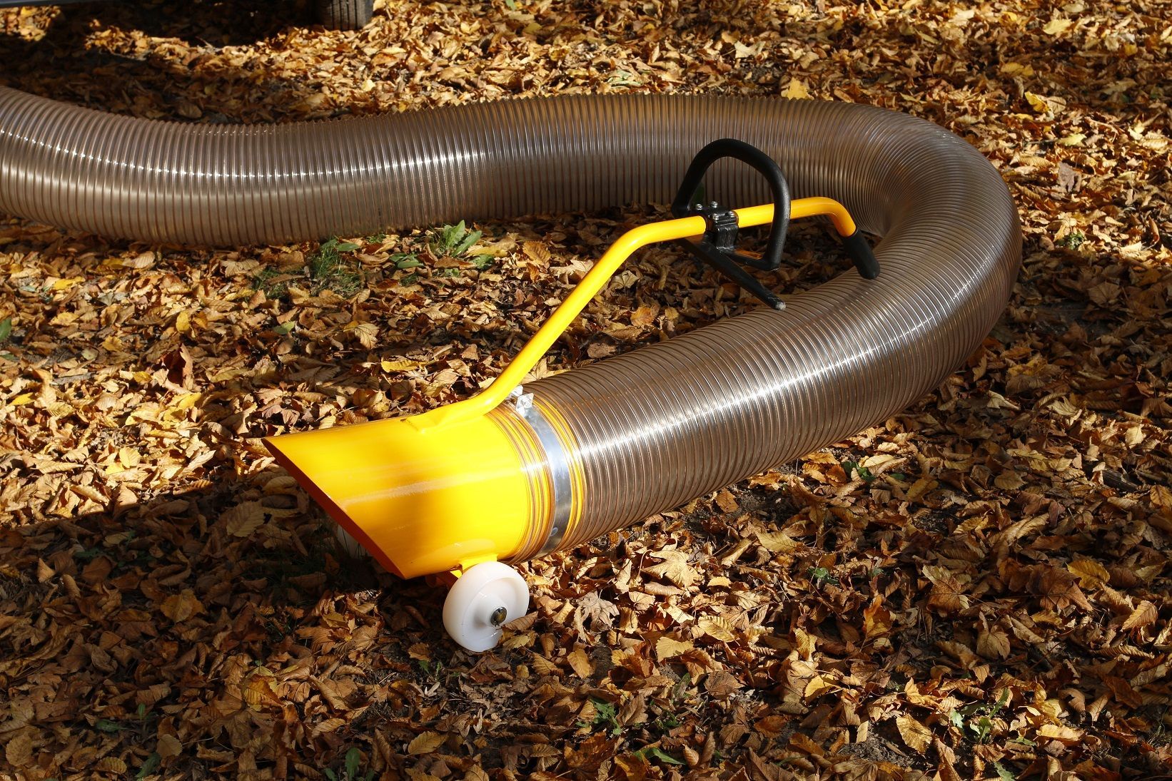 Auf einem Laubhaufen liegt ein Schlauch mit gelber Spitze.