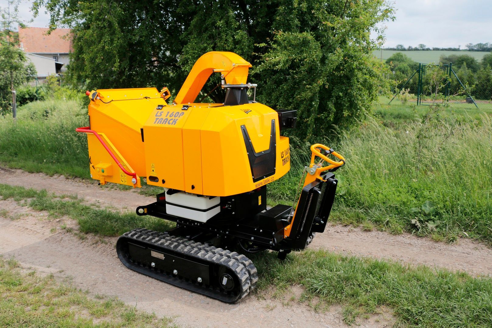 Eine kleine gelbe Maschine ist auf einem Feldweg neben einem Baum geparkt.