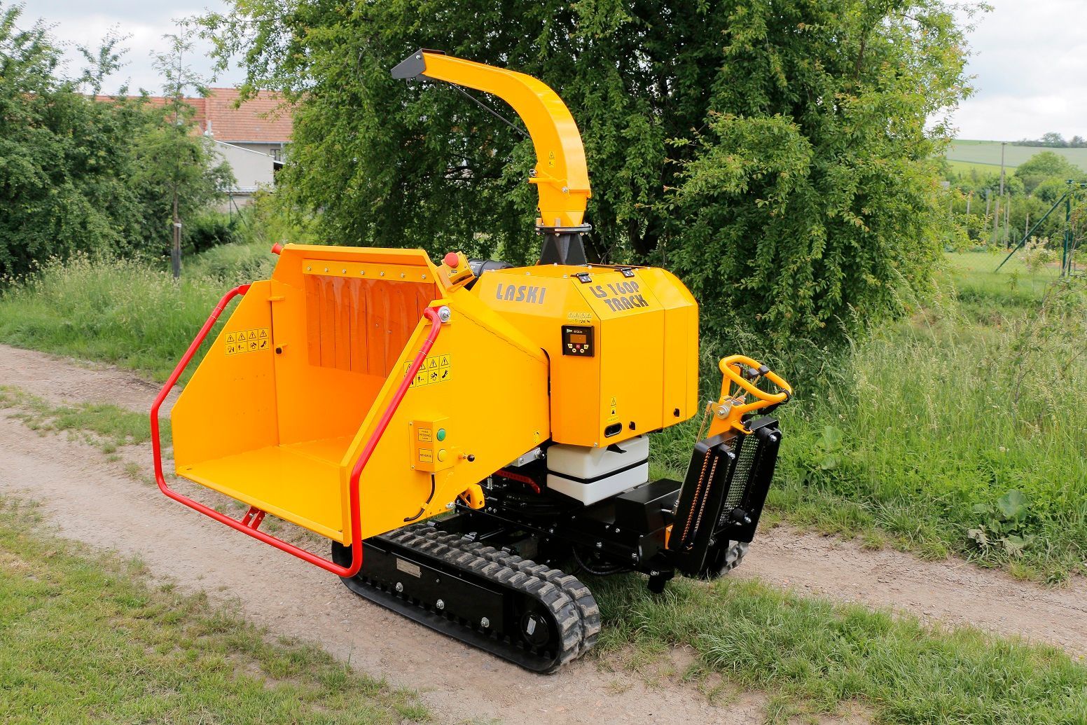 Eine gelbe Maschine steht auf einem Feldweg neben einem Baum.