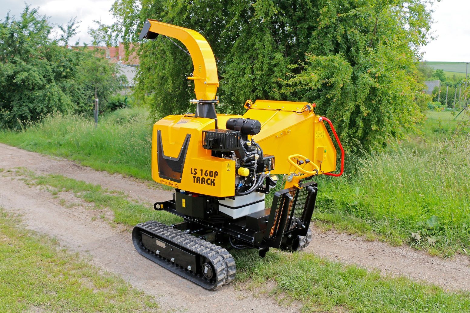 Ein gelber Baumhäcksler steht am Rand einer unbefestigten Straße.