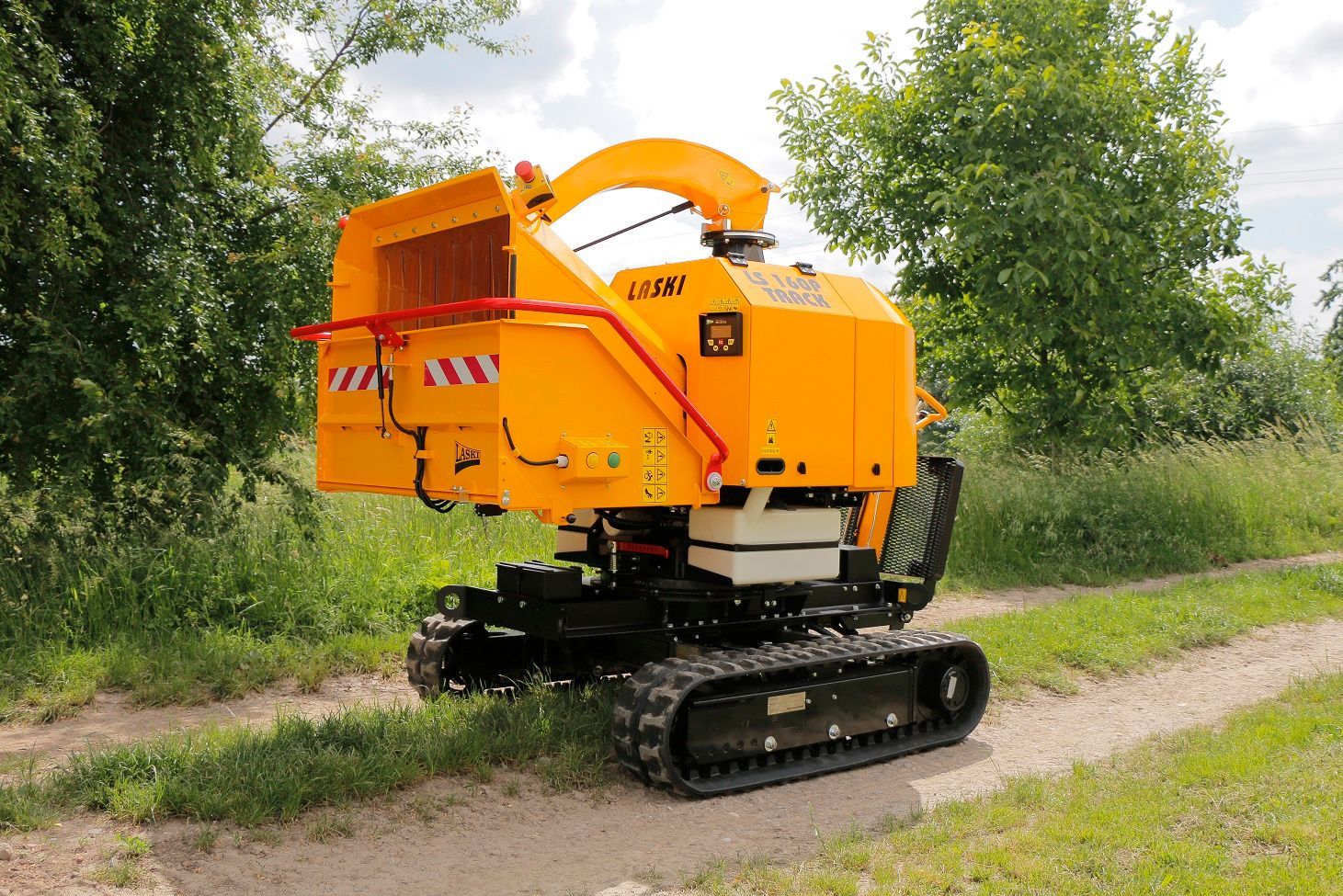 Eine gelbe Maschine steht auf einem Feldweg neben Bäumen.