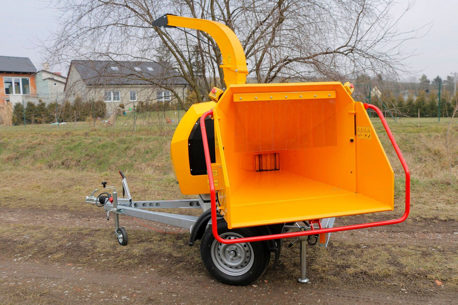 Auf einem Feld steht ein gelber Baumhäcksler auf einem Anhänger.