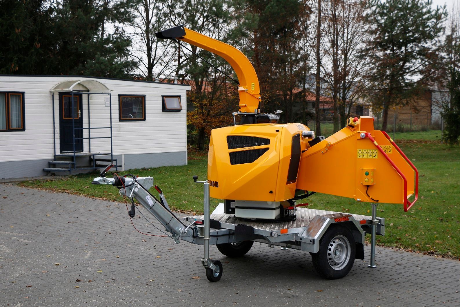 Eine gelbe Maschine steht auf einem Anhänger vor einem Wohnmobil.