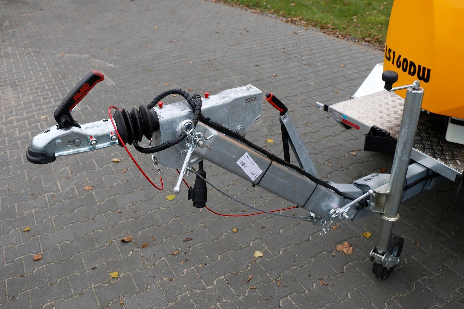 Auf einer Ziegelsteinstraße ist ein Anhänger an einen gelben Traktor angehängt.