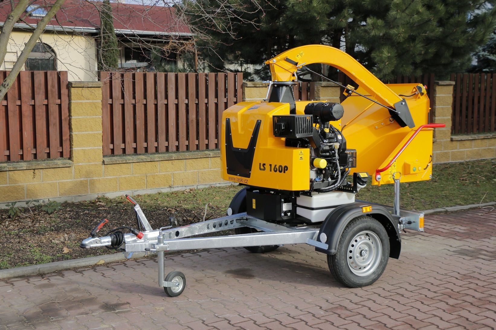 Eine gelbe Maschine steht auf einem Anhänger vor einem Zaun.