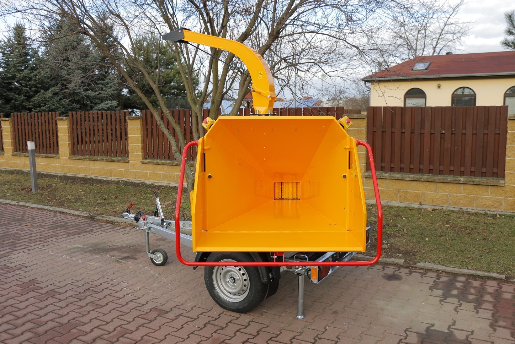 Ein gelber Baumhäcksler steht auf einem Anhänger vor einem Haus.