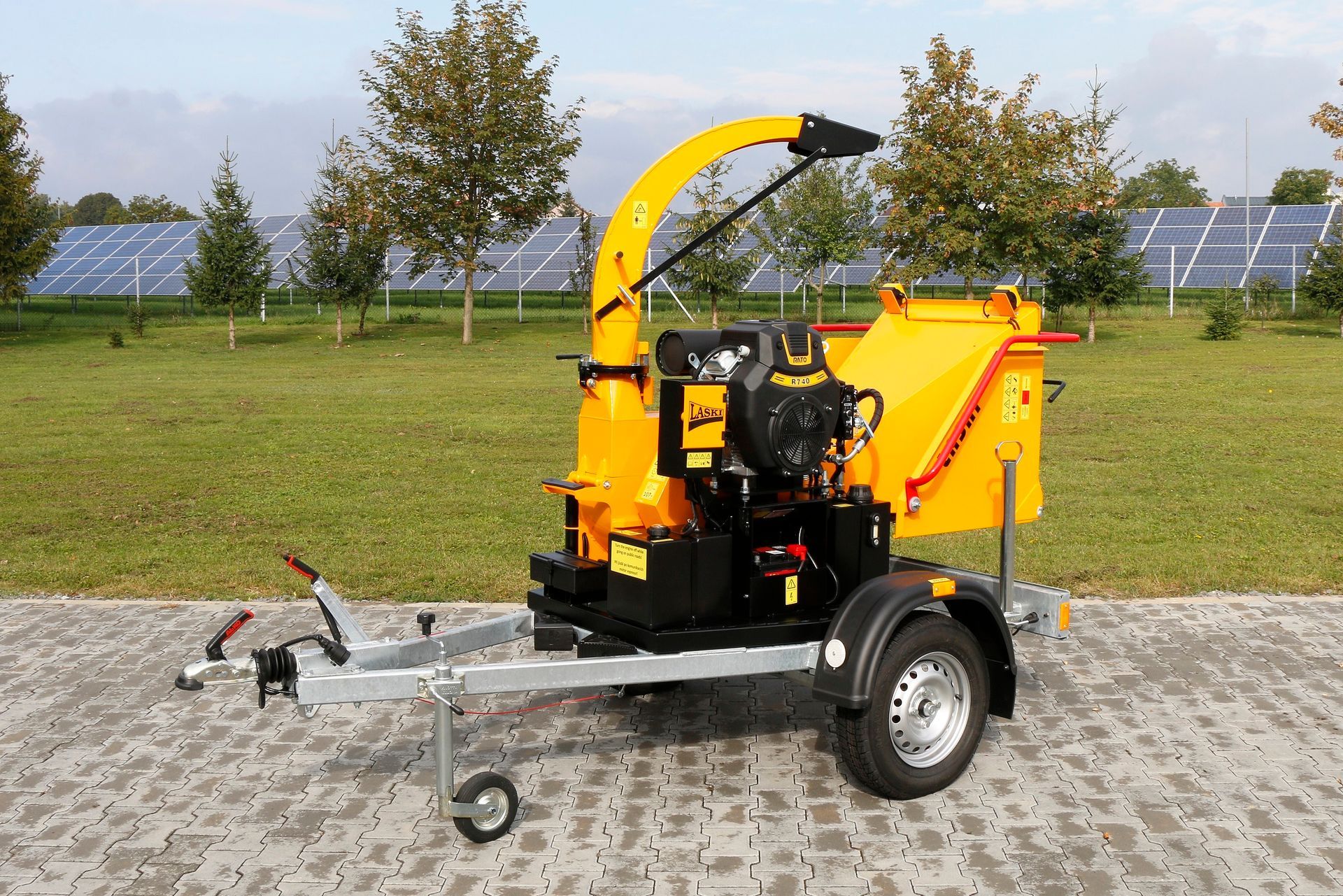 Auf einem Bürgersteig steht ein gelber Baumhäcksler auf einem Anhänger.