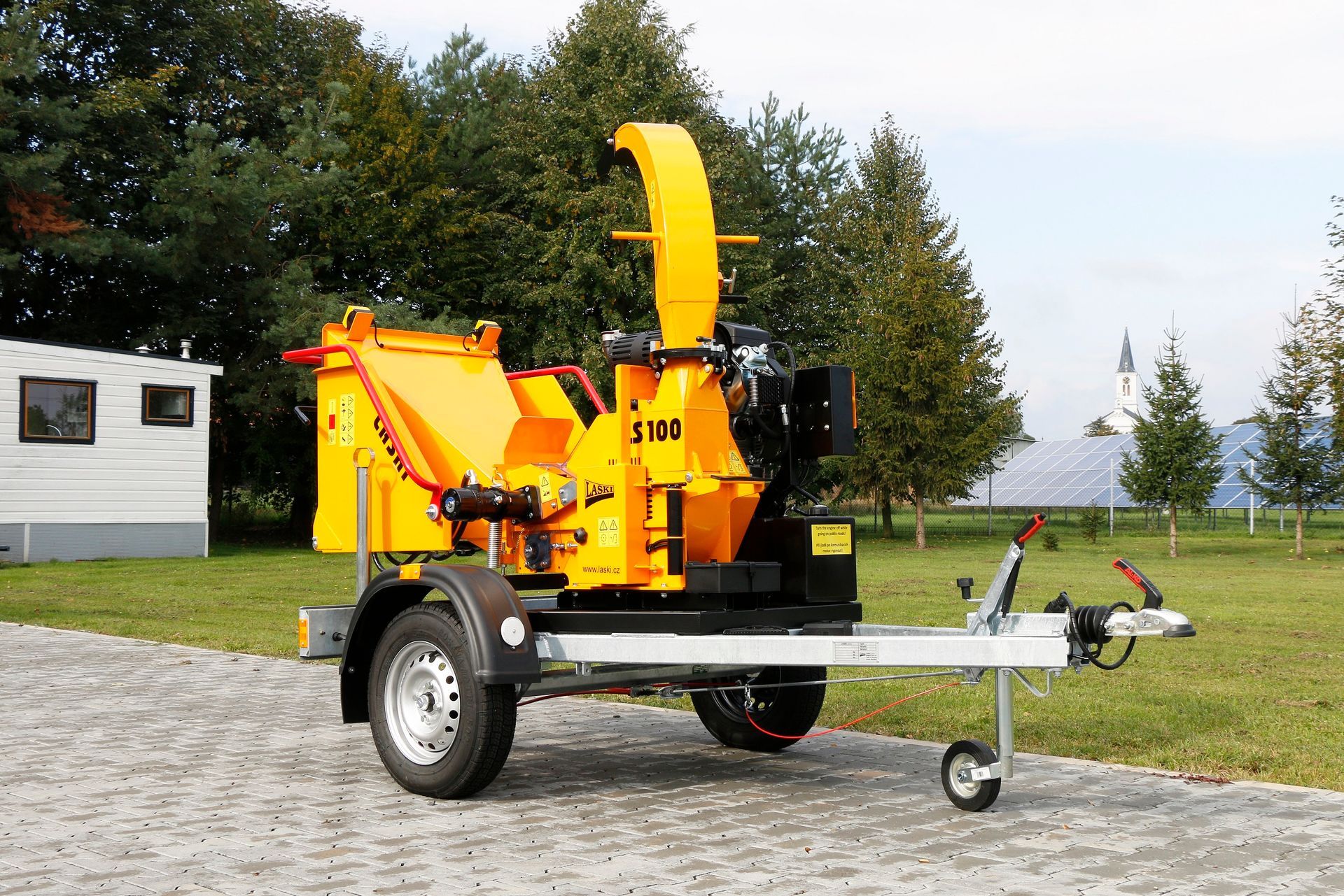 Eine gelbe Maschine steht auf einem Anhänger vor einem Haus.