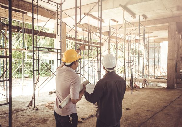 Two construction workers are looking at a blueprint at a construction site.