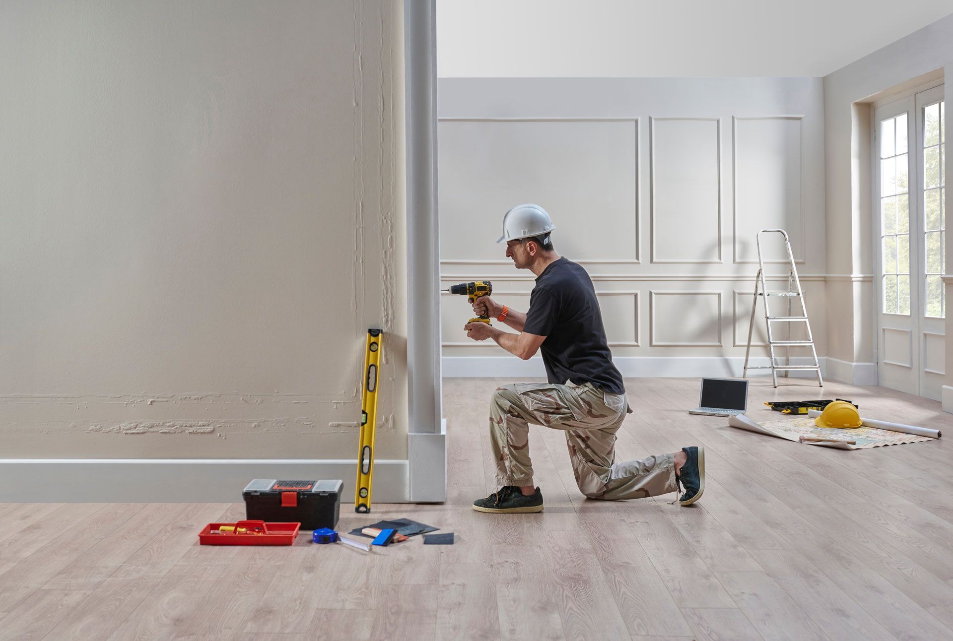 A man is kneeling down in an empty room using a drill.