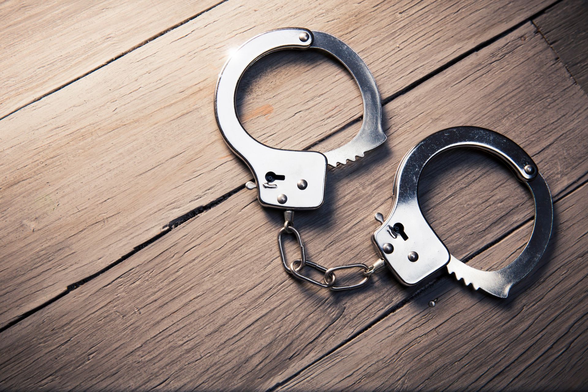 A pair of handcuffs are sitting on a wooden table.