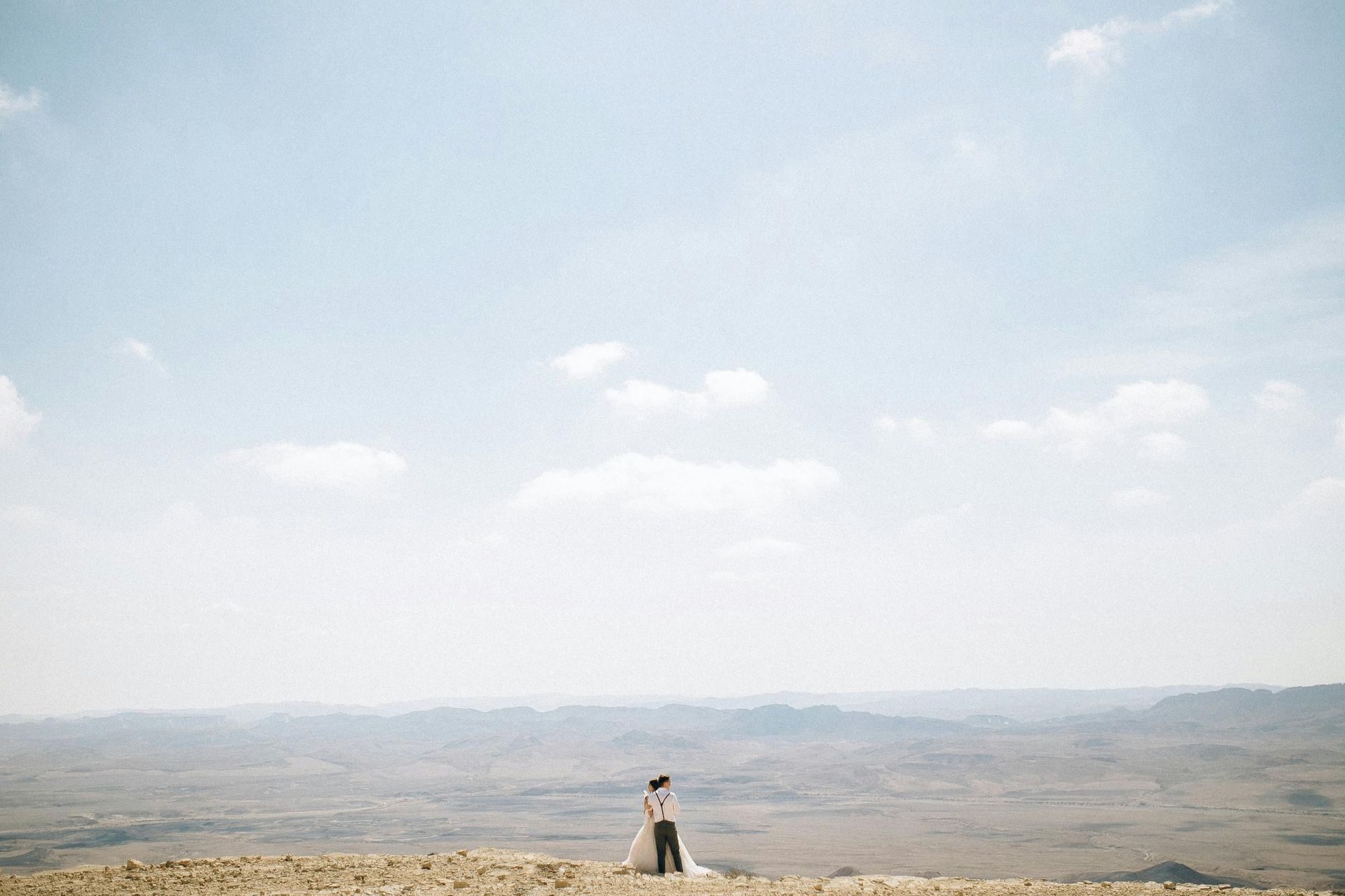 A bride and groom are standing on top of a hill in the desert.