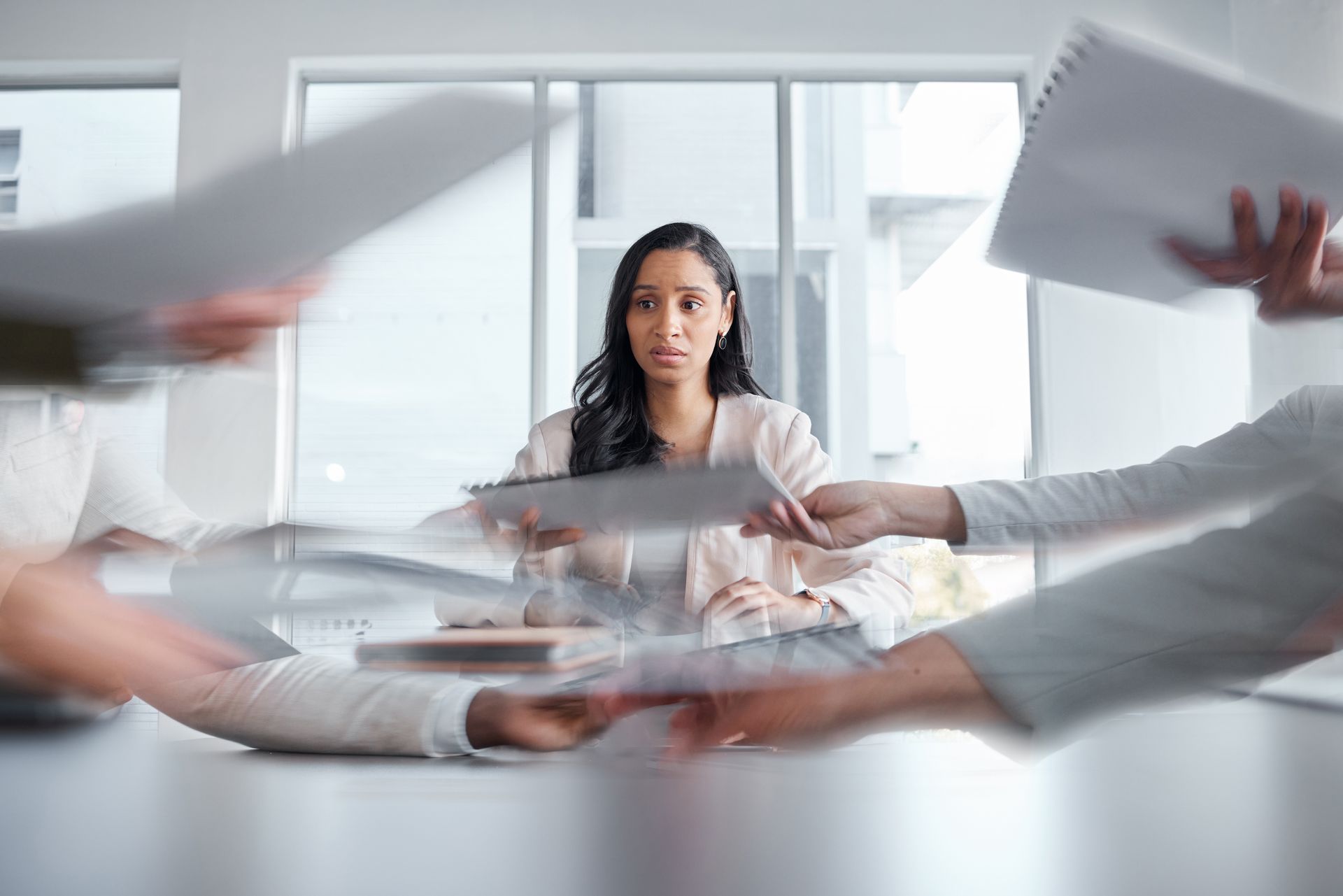 Woman seated at a meeting table as papers are passed around her in a bright office