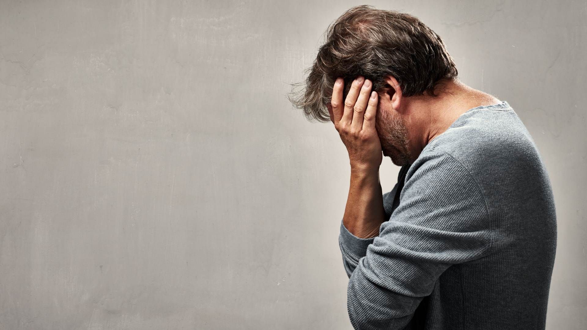 Person sitting with head in hands against a gray background, appearing stressed or upset