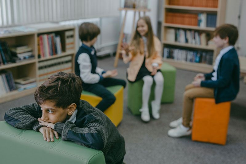 A group of children are sitting on ottomans in a library.