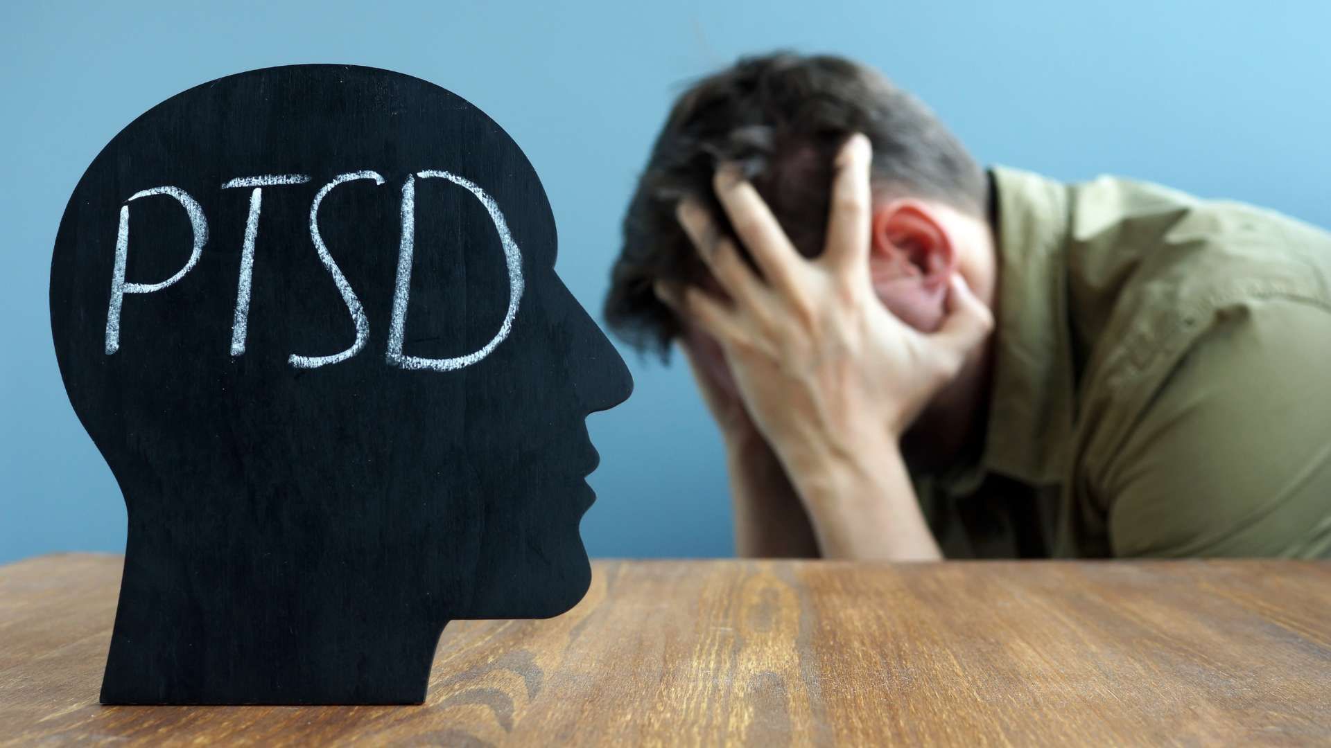 Silhouette labeled “PTSD” facing a distressed person holding his head at a table