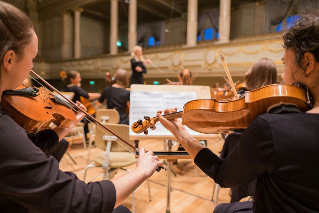 Two women are playing violins in an orchestra.