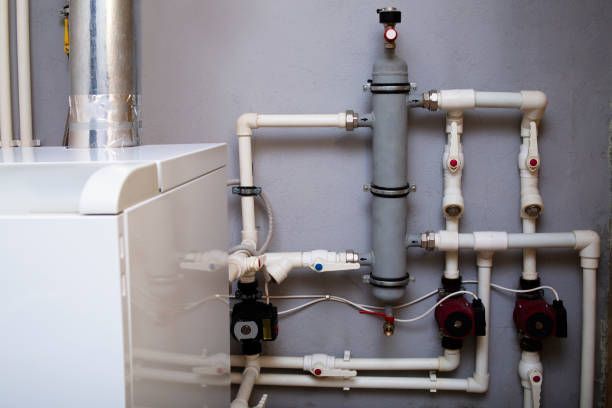 White pipes and a boiler connected to red pumps against a gray wall.