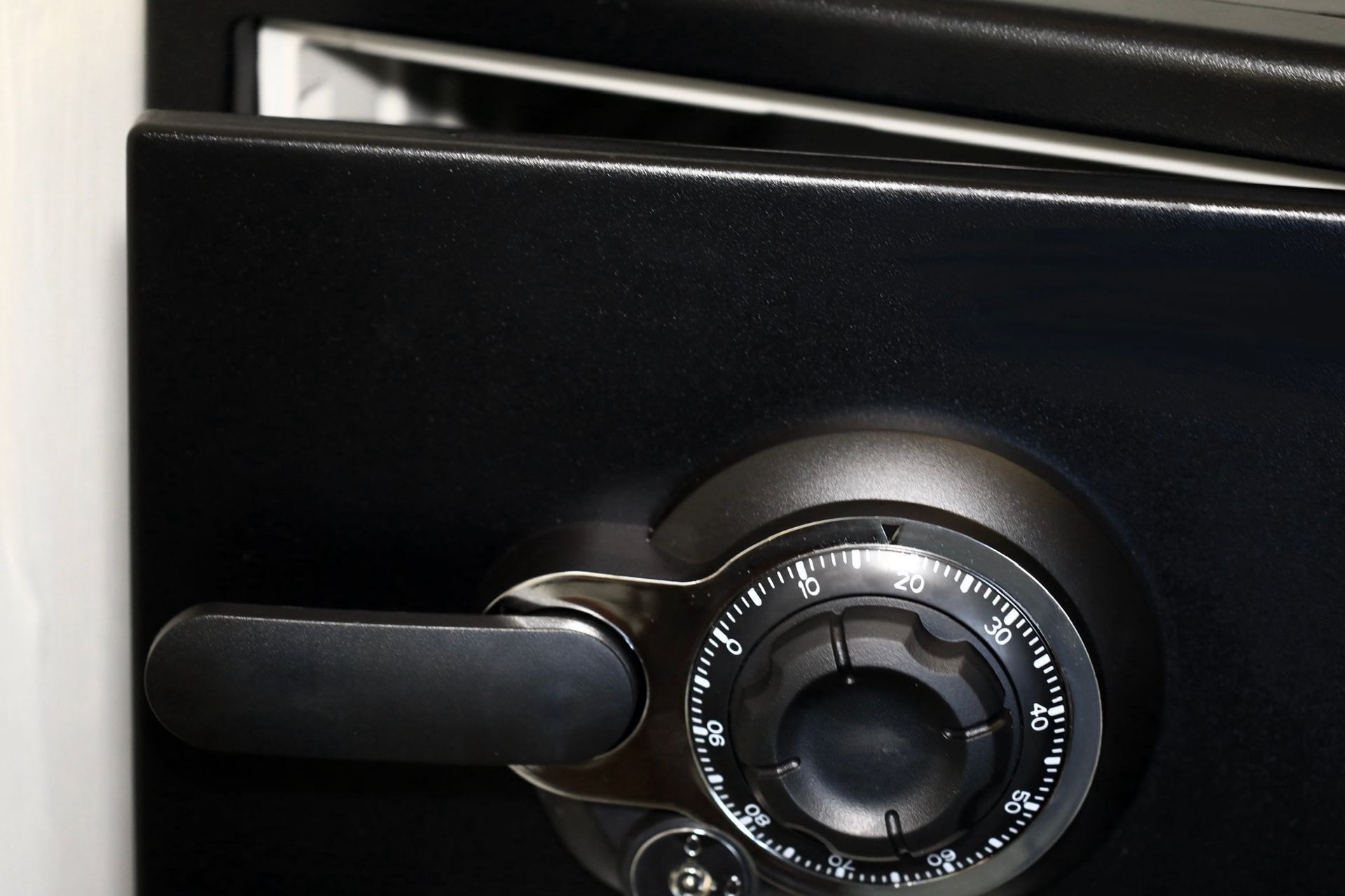 Black safe with a combination dial and handle, the door slightly ajar.