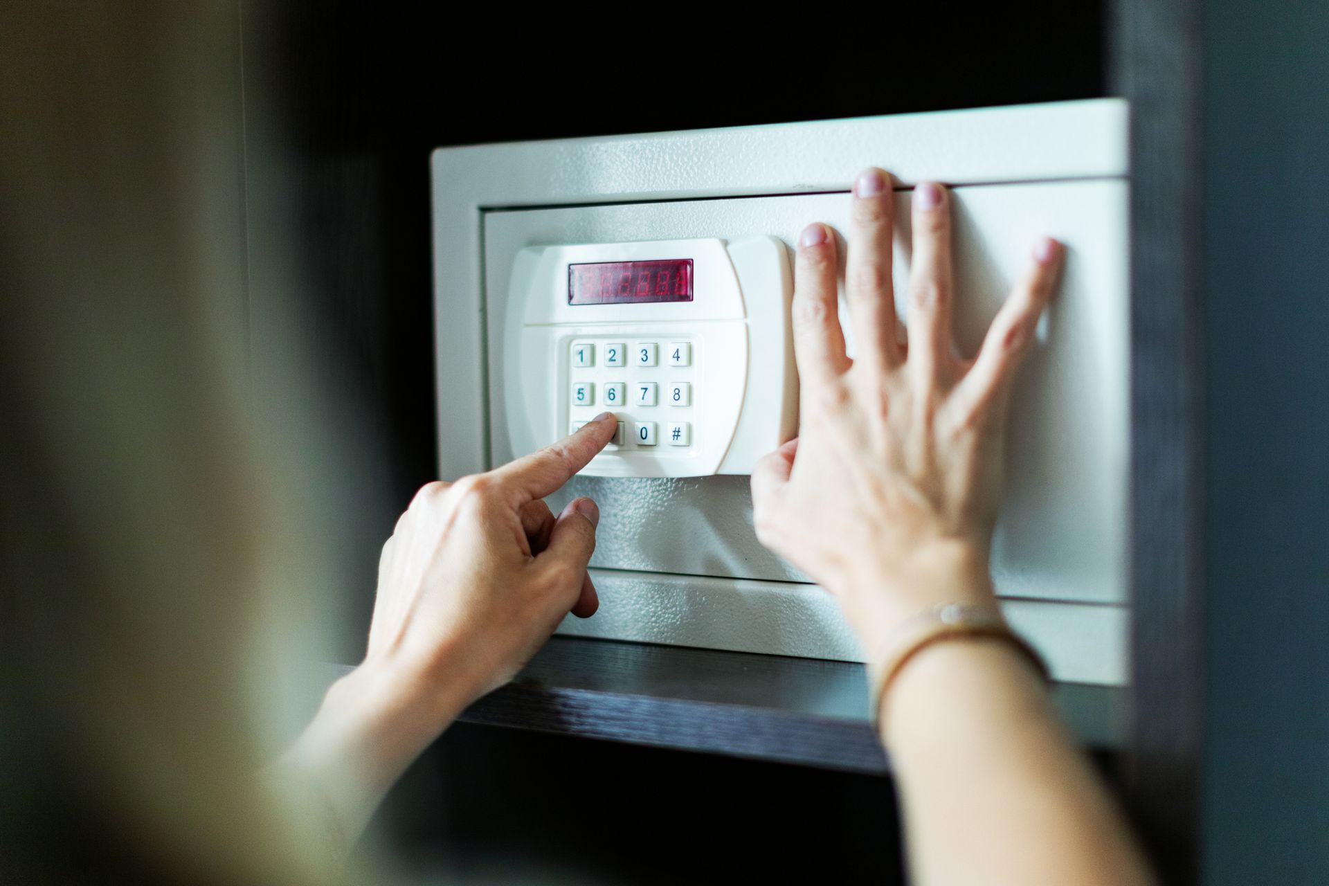 Person's hands opening a white safe with a keypad. The safe is in a dark cabinet.