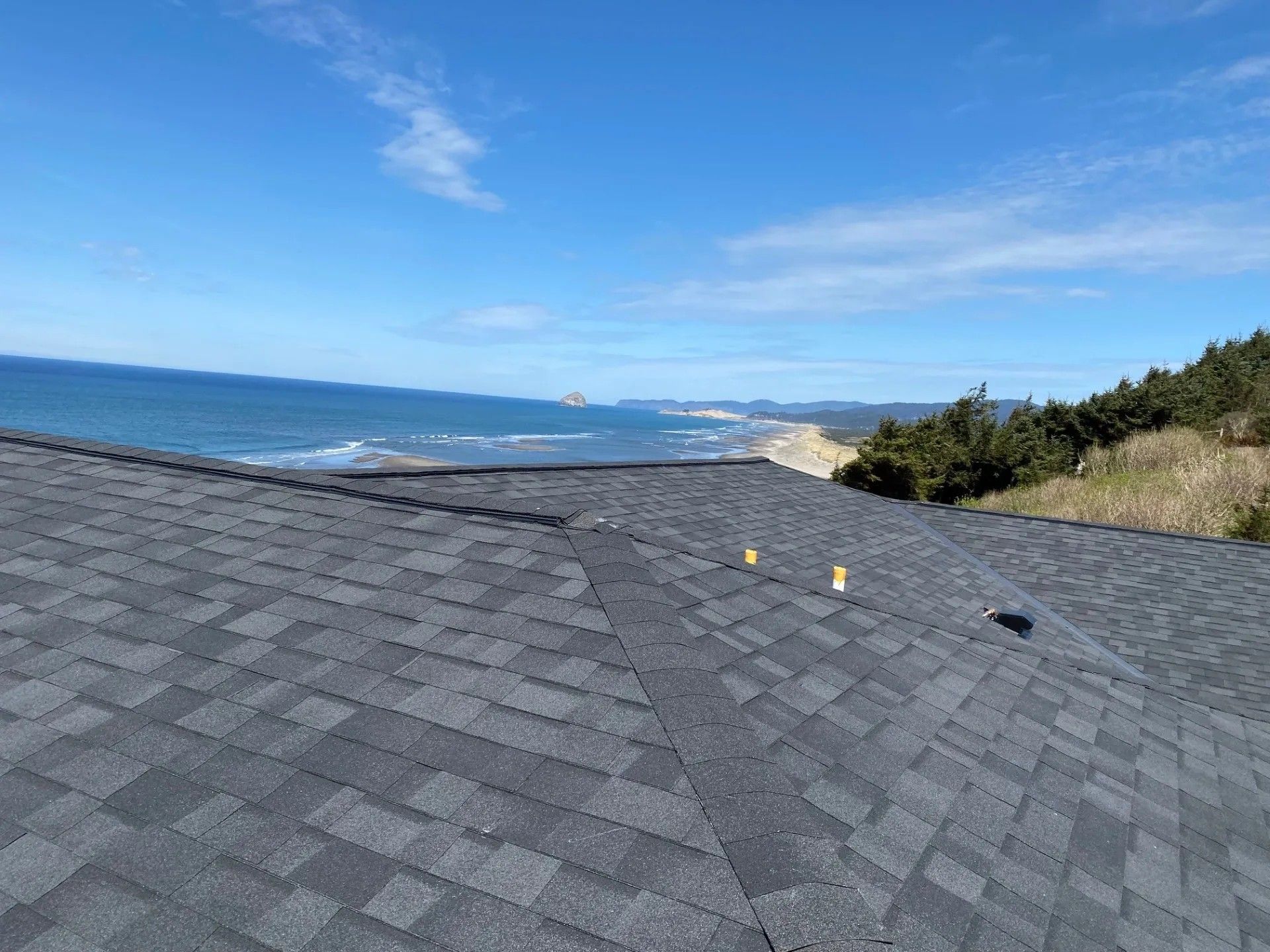 A view from a gray shingled roof overlooking a blue ocean and coastline under a clear sky.