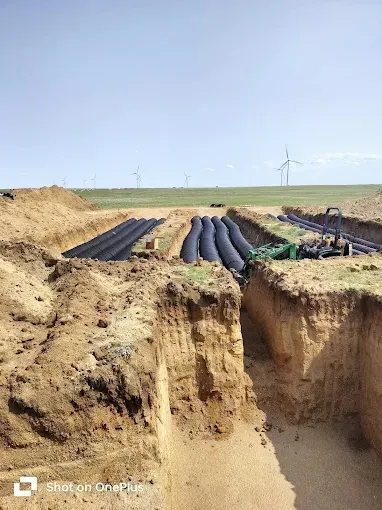 A bunch of pipes are laying in the dirt in a trench.