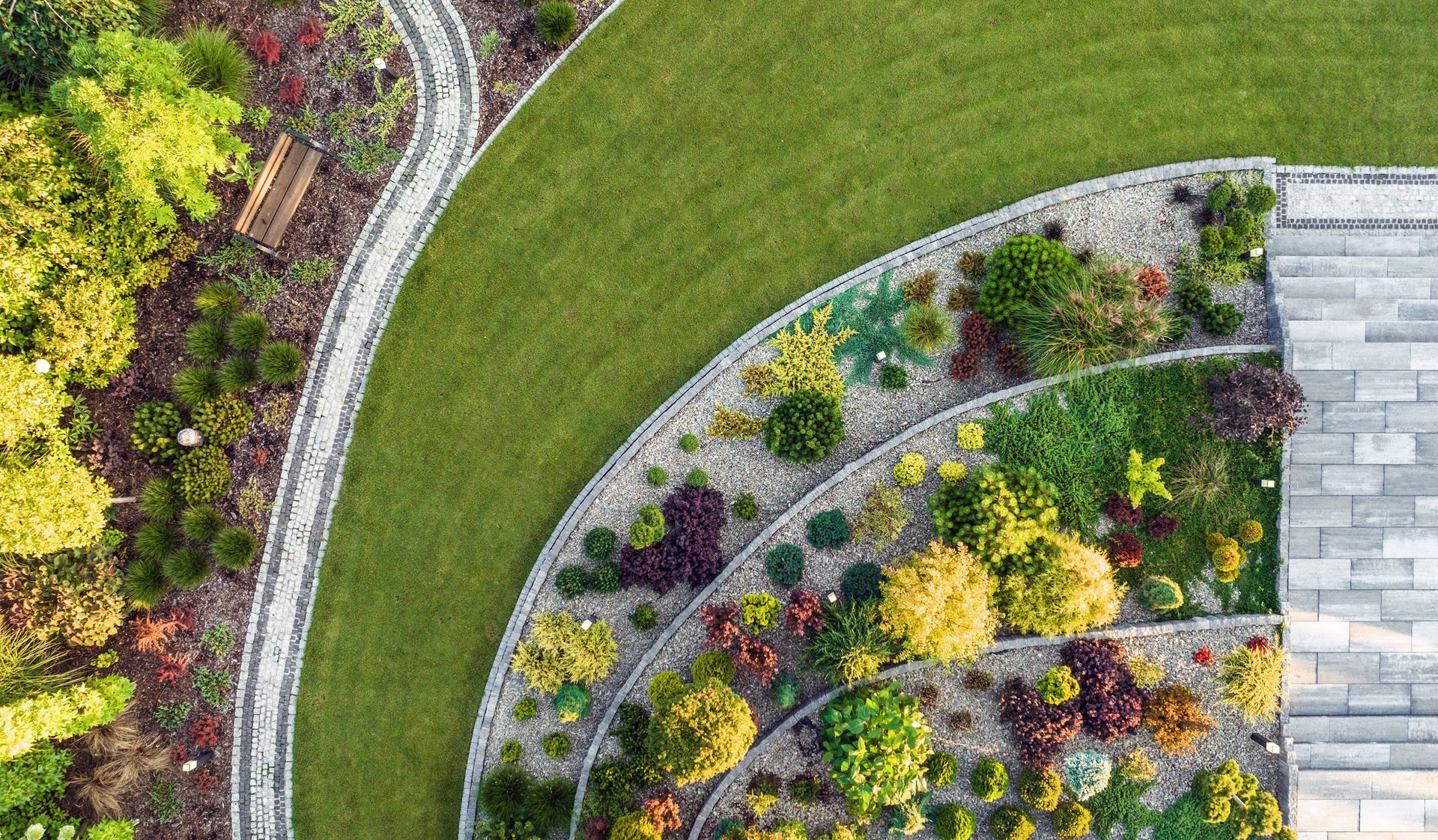 Overhead view of a tiered garden bed with lush plants, stone edging, and a green lawn.