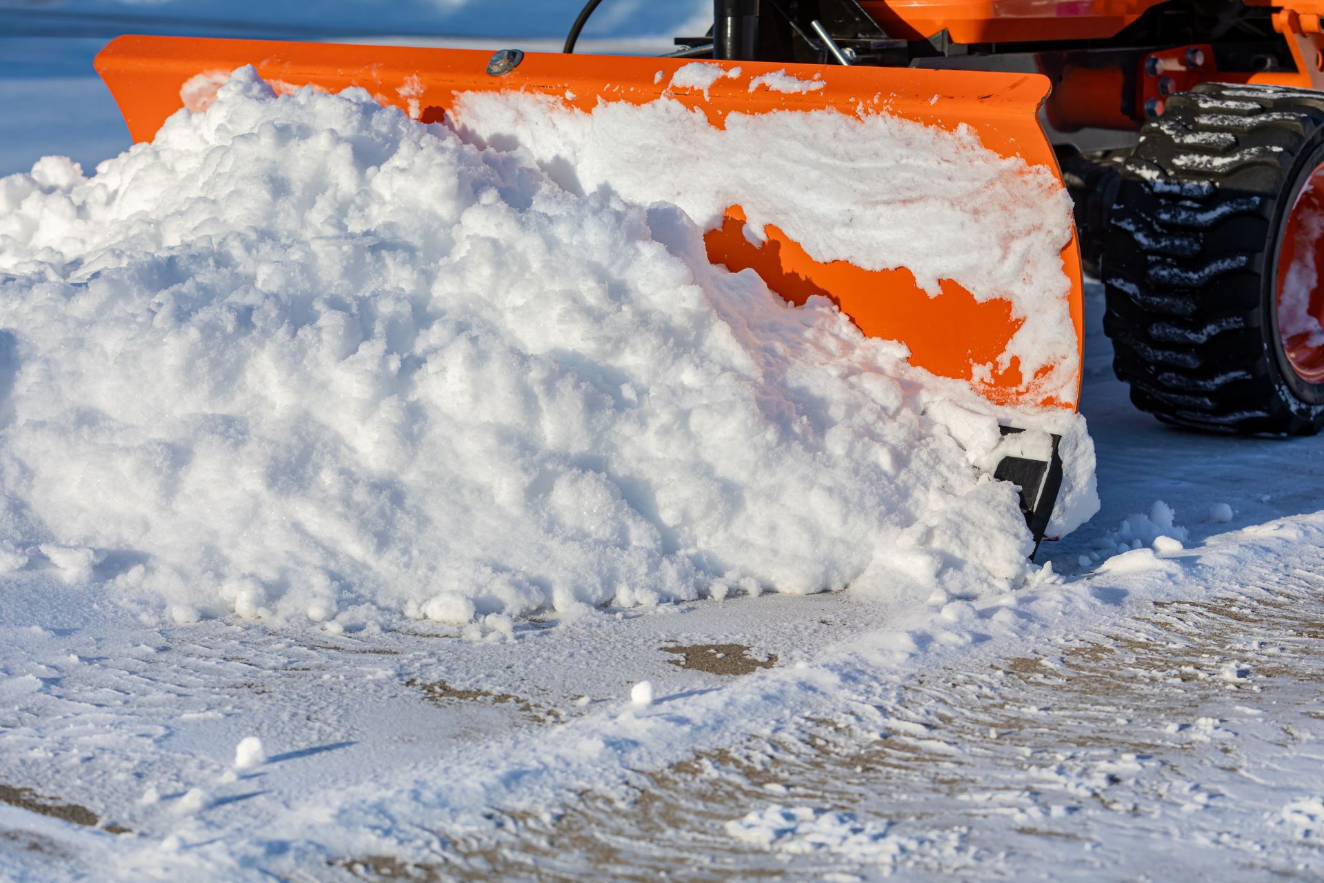 Orange snowplow pushing a pile of white snow on a paved surface.