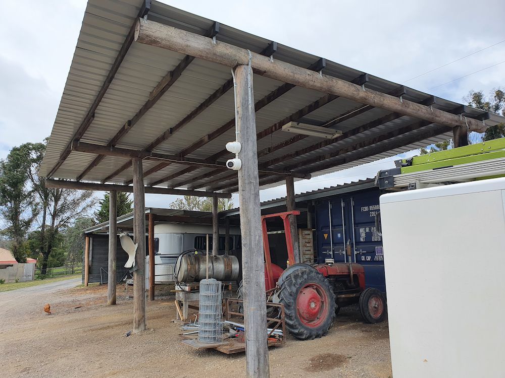 Outdoor Rural Shed With a Red Tractor Underneath, Featuring a Mounted CCTV Security Cameras — AitkenTech in Batemans Bay, NSW