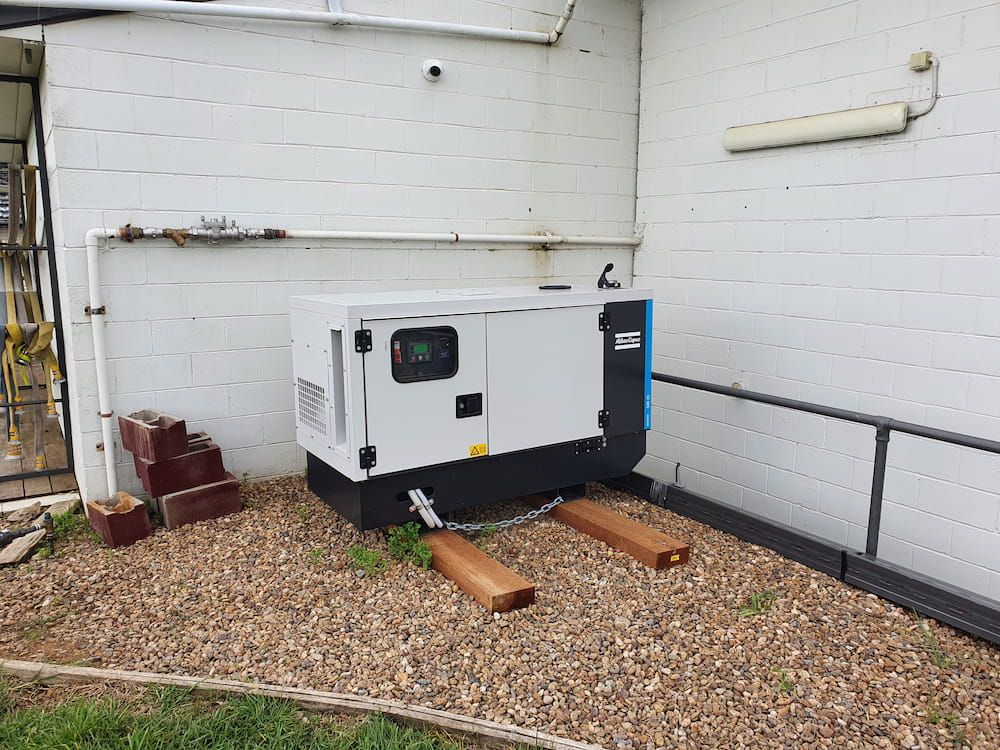White Generator Secured With Chains Next to Brick Wall — AitkenTech in Batemans Bay, NSW