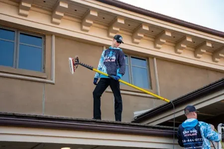 Person in yellow raincoat power washing a gray house.