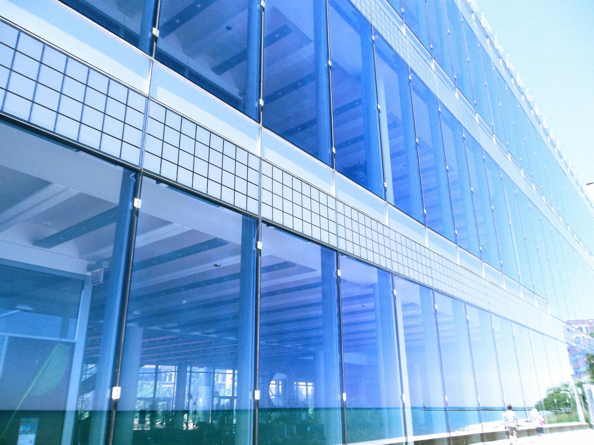 Blue glass building exterior with reflective windows, clear sky.